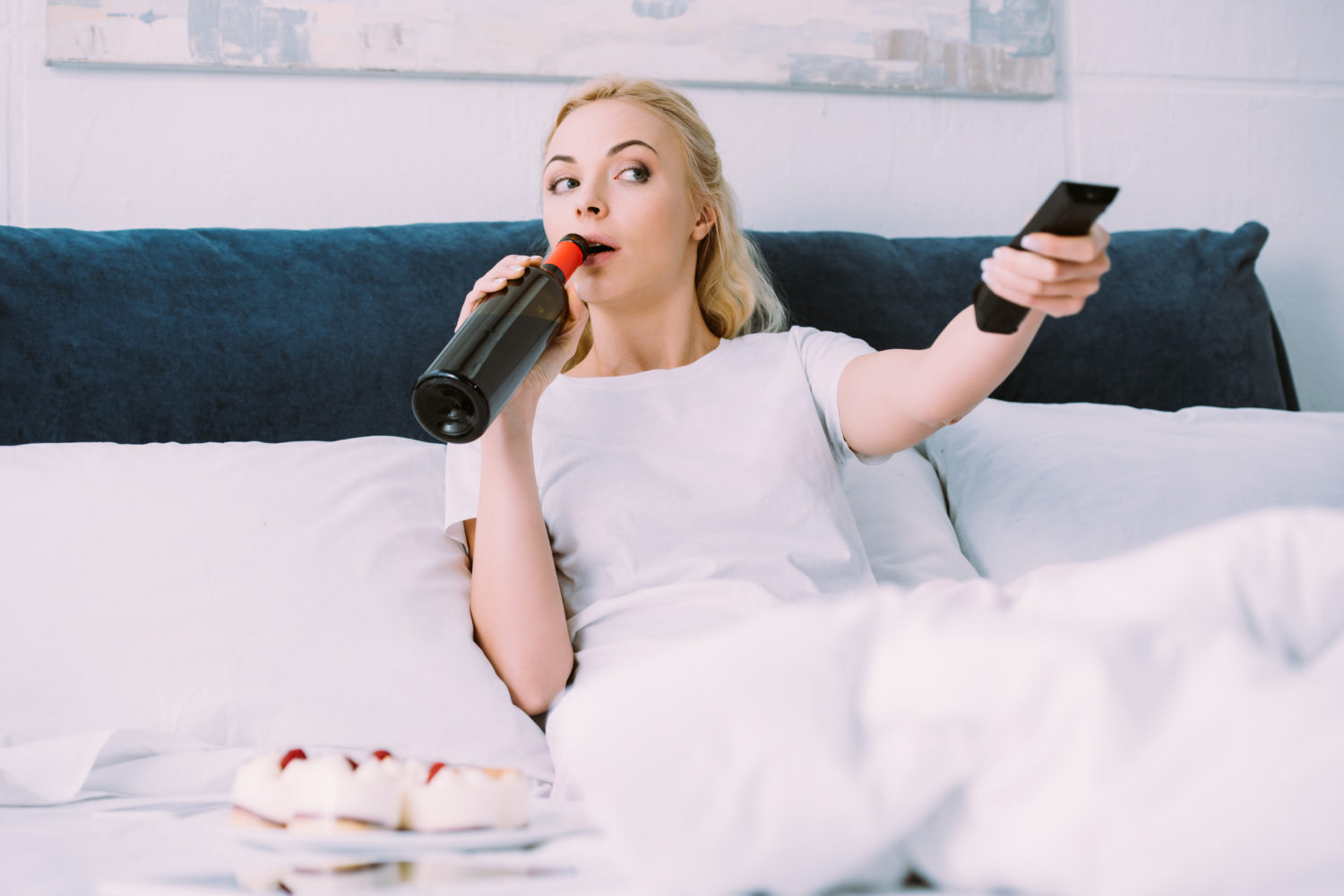 woman drinking wine and watching tv while celebrating birthday in bed alone